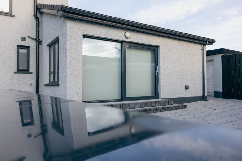 Anthracite grey two-pane sliding patio door on a white rendered single-storey rear extension, with brick steps down to a paved patio