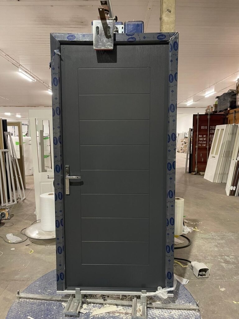 Anthracite grey solid front door with horizontal grooved panels and a lever handle, on the wrapping turntable in the factory
