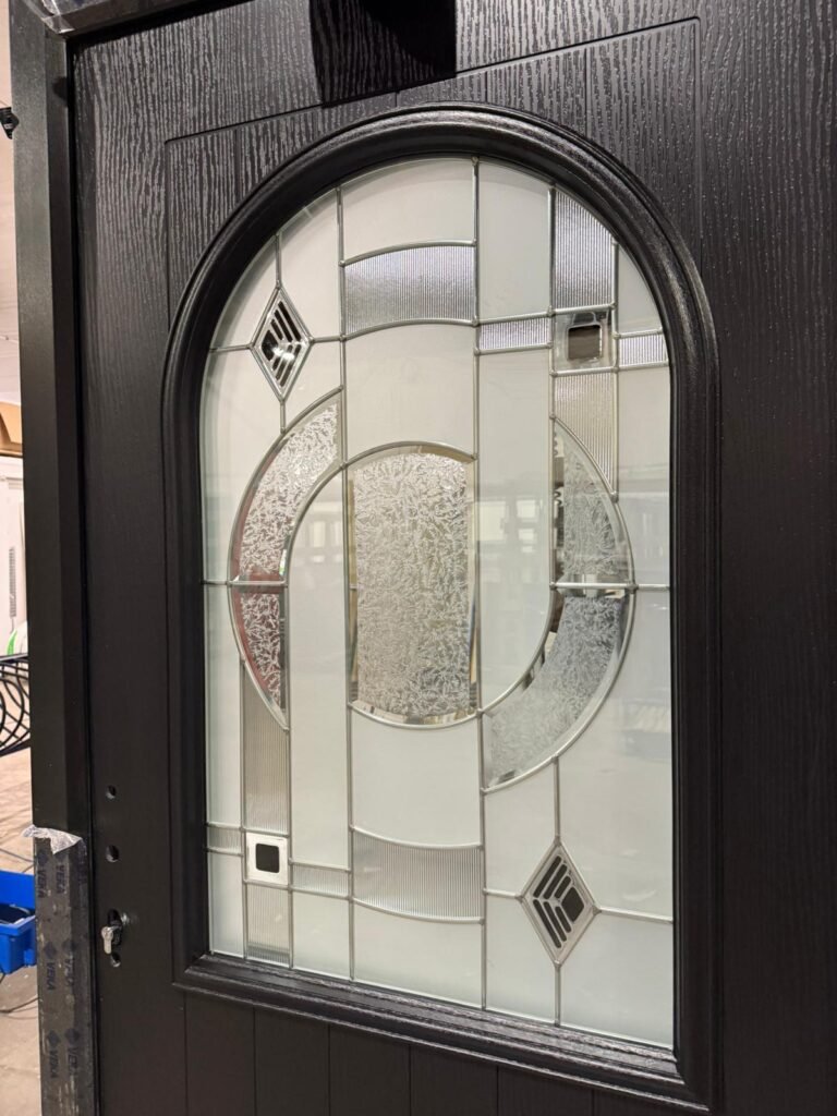 Close-up of a black woodgrain door with a large arched panel of decorative leaded and textured glass