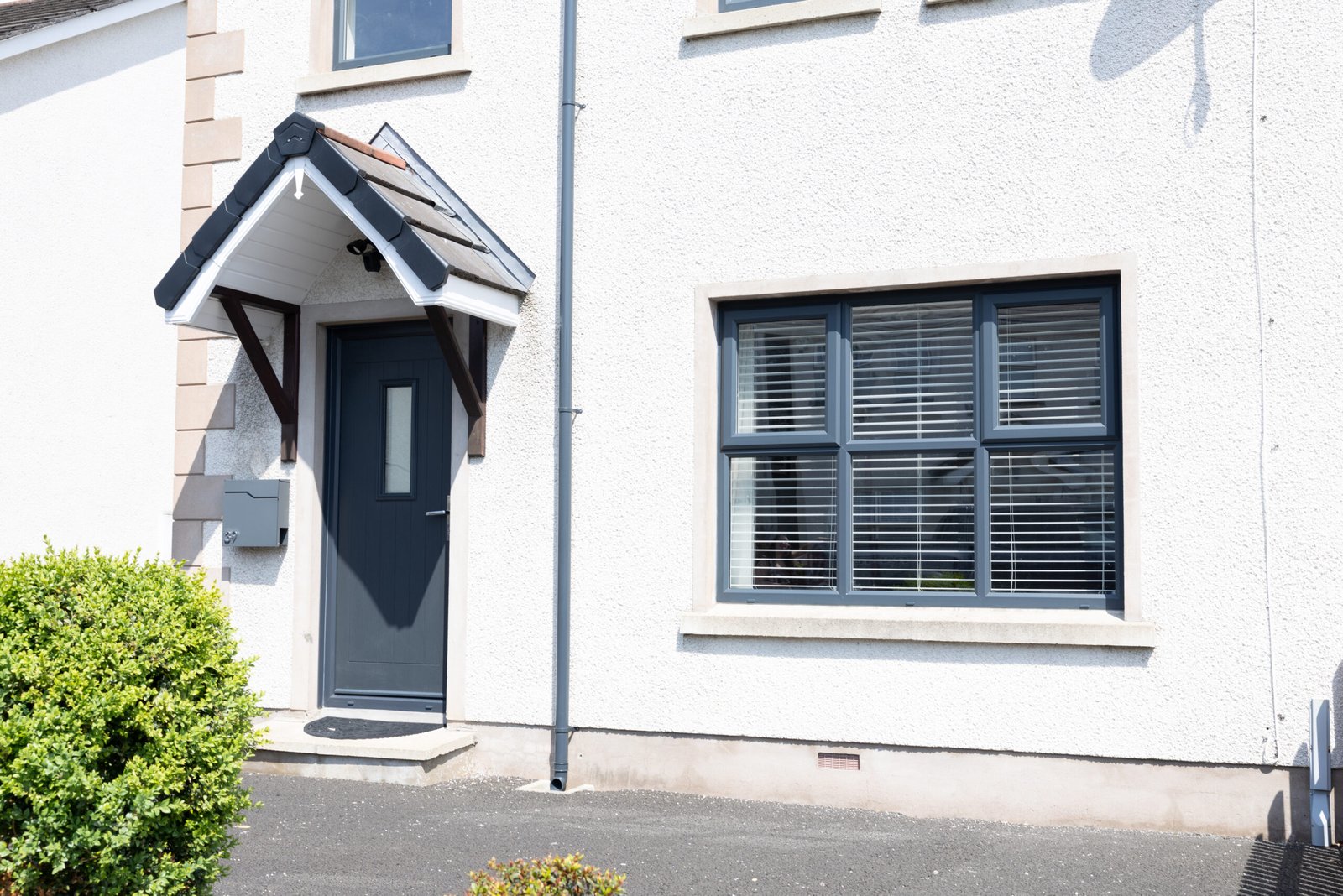Anthracite grey composite front door and grey uPVC casement windows on white render house