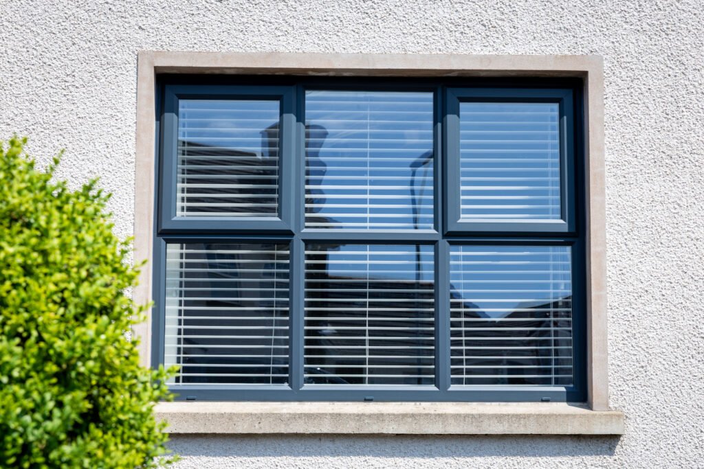 Anthracite grey uPVC six-pane casement window with stone cill on white render exterior