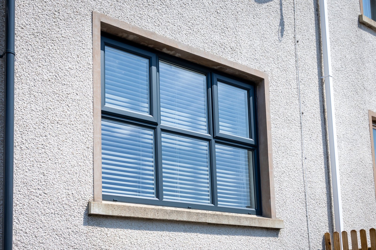 Anthracite grey uPVC six-pane casement window with stone surround on white render wall