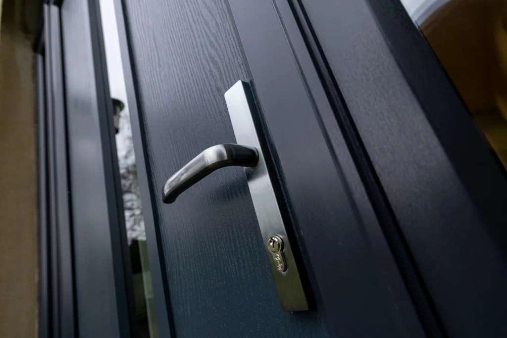 Chrome lever handle detail on dark grey wood-grain textured composite entrance door