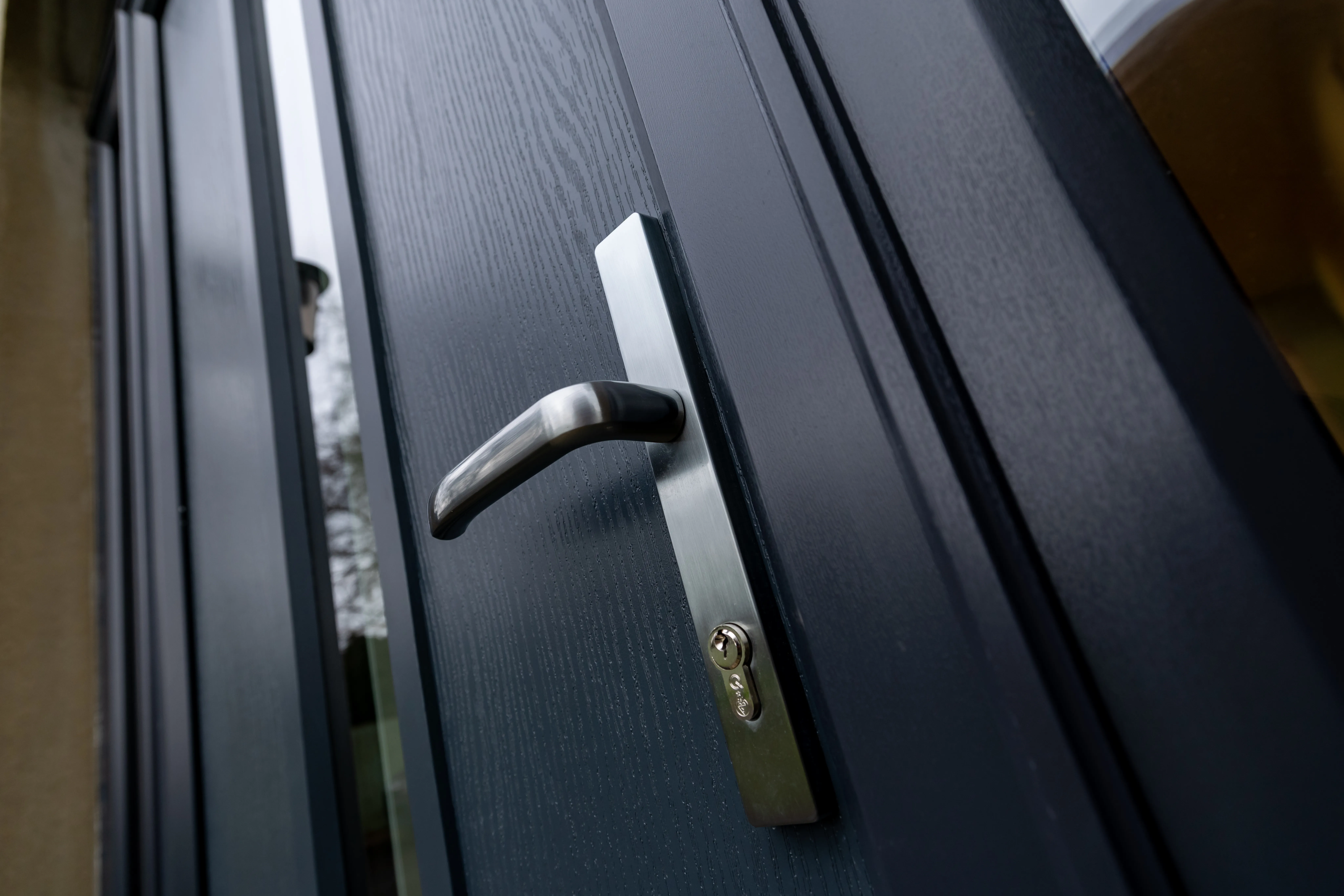 Close up of a brushed metal lever handle and lock on an anthracite grey door