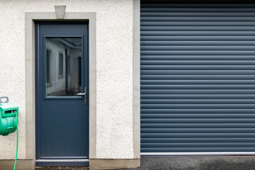 Anthracite grey half-glazed side door with a lever handle in a stone surround, beside a grey roller shutter garage door